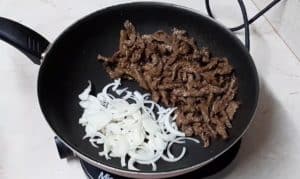 Place the shawarma in half of the pan and add the onion slices