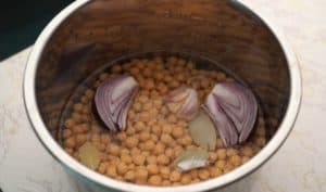 In a pressure cooker, put the chickpeas, cover with water, then add half an onion, a clove of garlic, two bay leaves and half a teaspoon of salt.